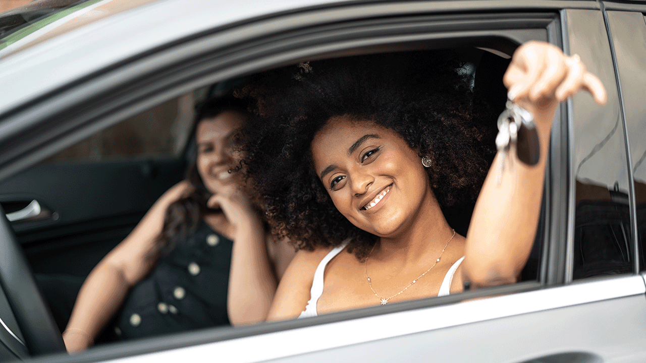 Pessoa sorrindo ao volante com as chaves do veículo
